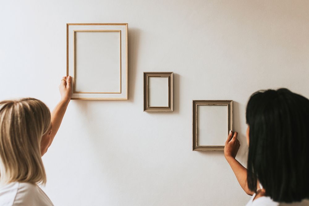 Two women styling frames on wall