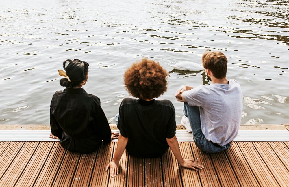 Three diverse friends sitting by the river bank 