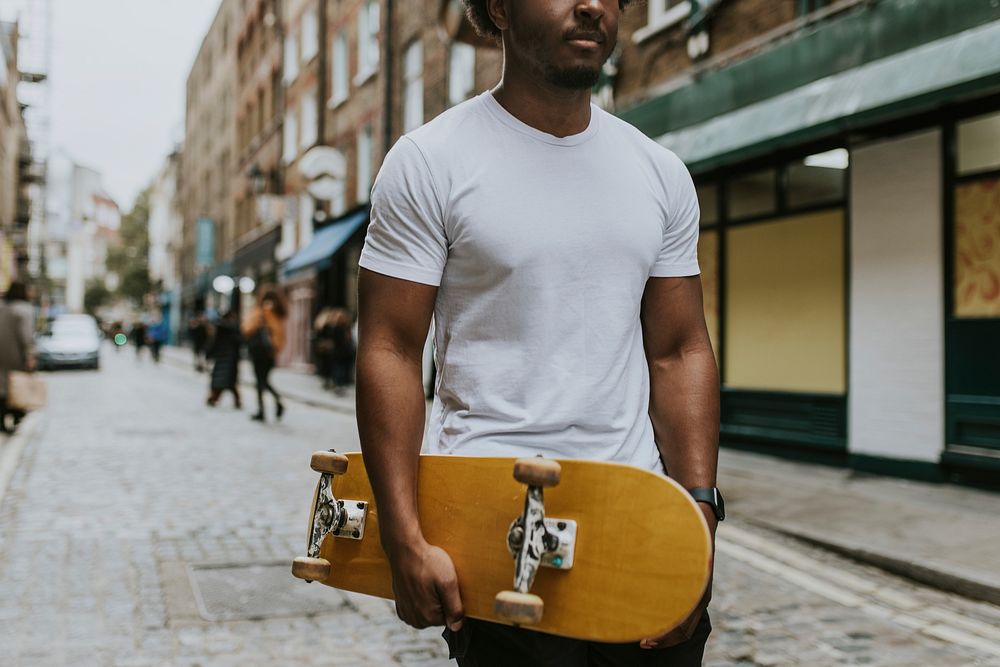 Man in white tee walking in town with wooden skateboard