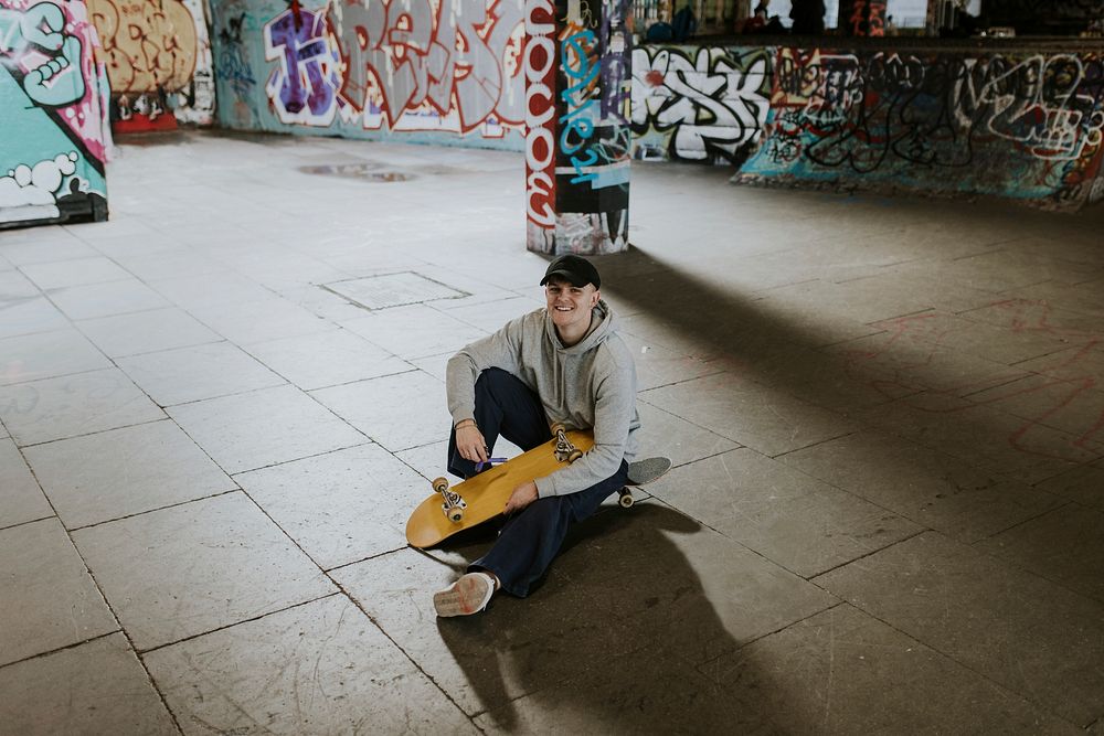 Man sitting in skate park with wooden skateboard