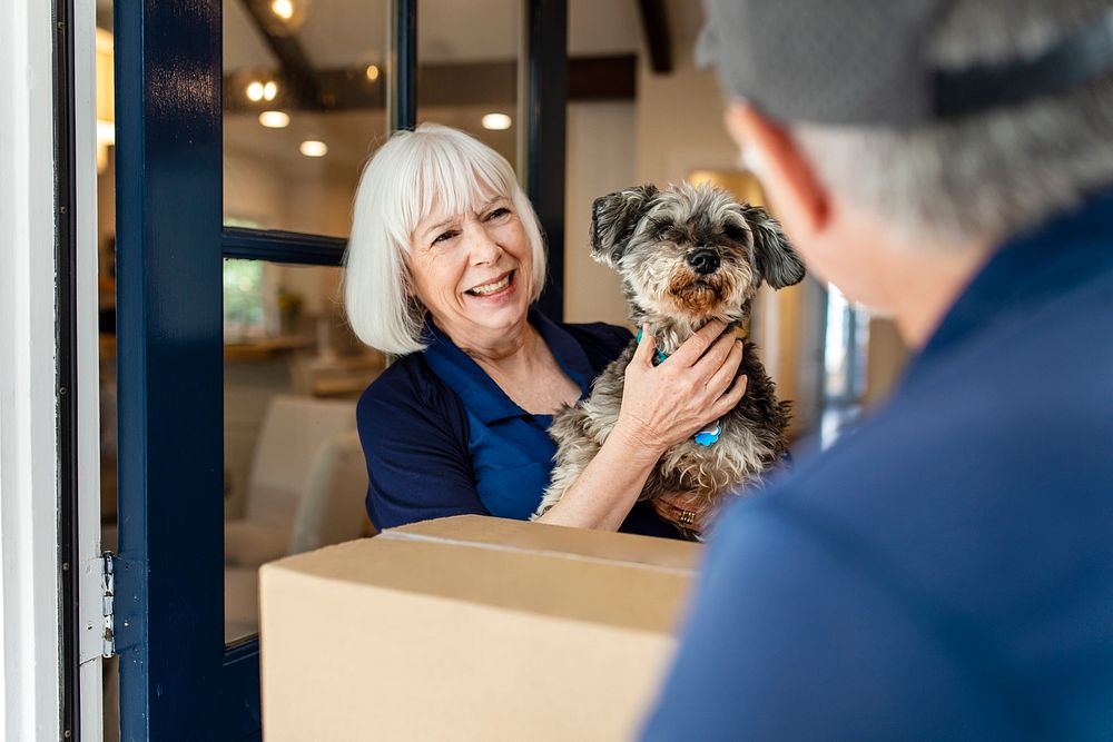 Senior woman receiving package delivery, holding a dog image