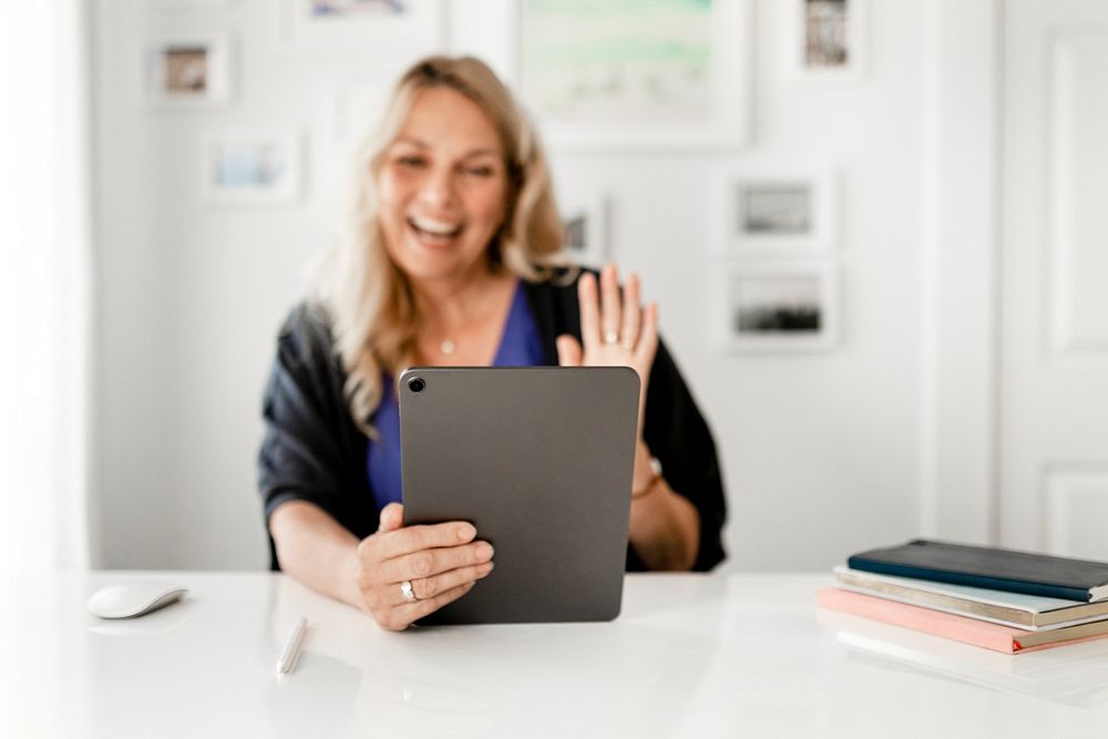 Woman waving during video call on tablet, business online meeting image