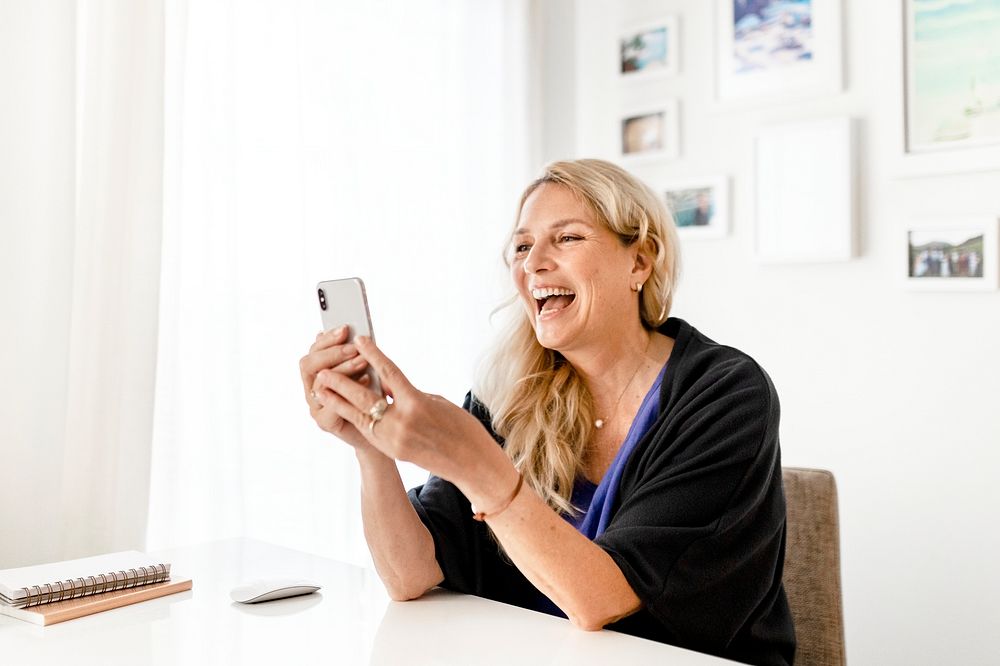 Blonde woman laughing, holding smartphone in her hand