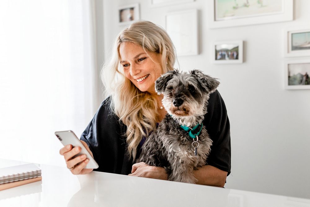 Smiling woman scrolling her phone, dog sitting on her lap