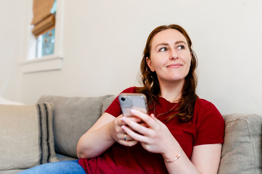 Brunette woman smiling, holding smartphone while sitting on a couch