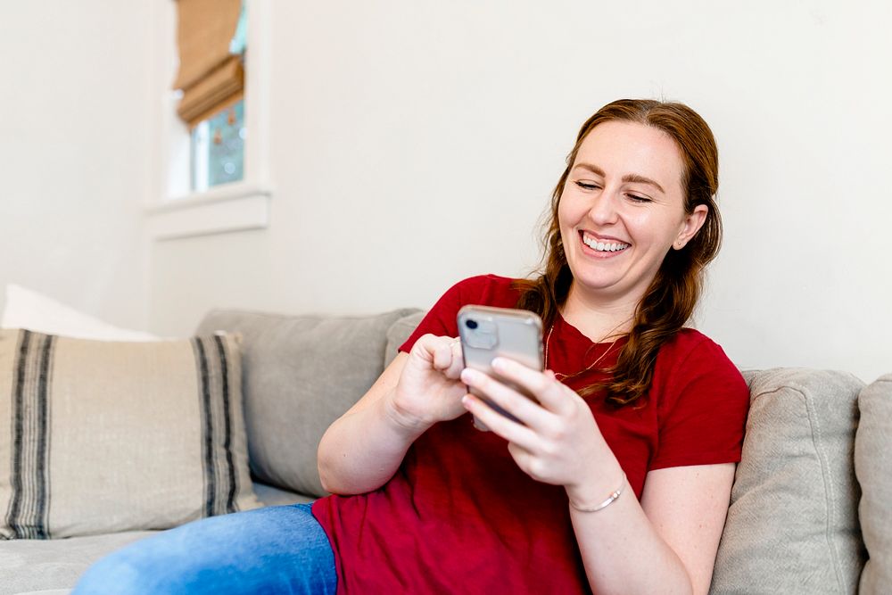 Woman laughing while texting, sitting on a couch in the living room