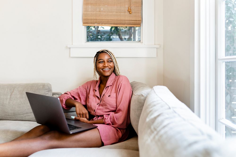 Happy black woman with laptop, sitting on the couch at home 