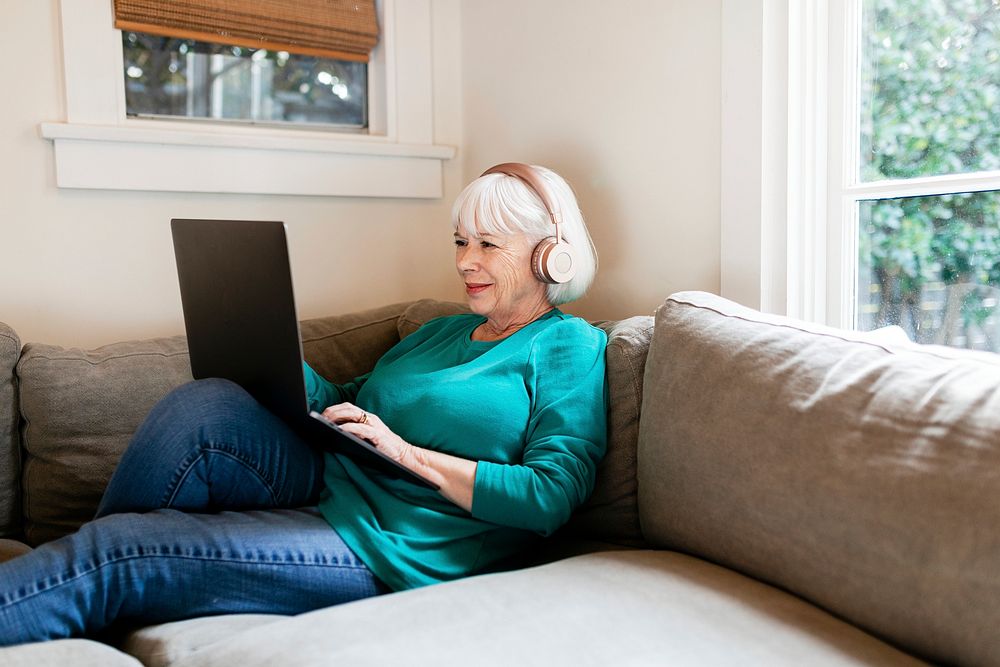 Senior woman using laptop, surfing the internet with headphone on