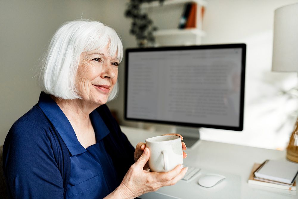Senior woman holding mug, relaxing in her home office