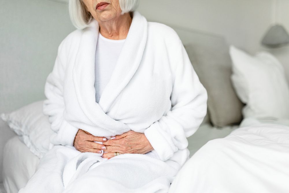 Senior woman with stomach pain, sitting on her bed