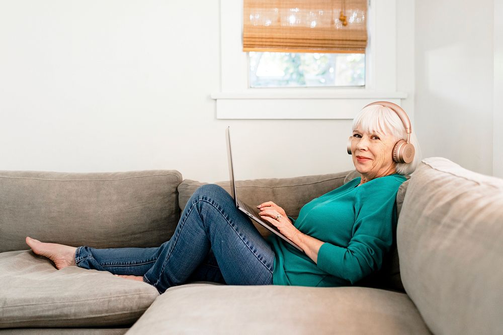 Happy old woman using laptop, sitting in living room at home