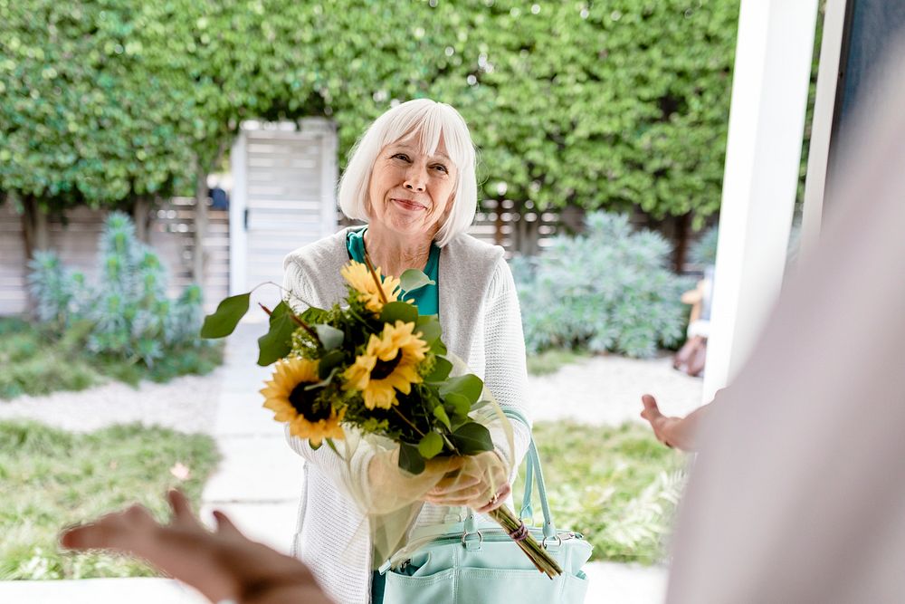 Senior woman holding sunflower bouquet, visiting neighbour