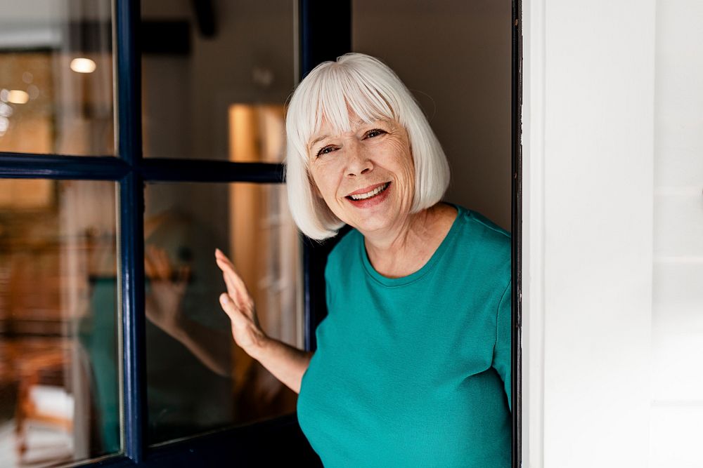 Smiling senior woman welcoming guest, retirement home doorstep