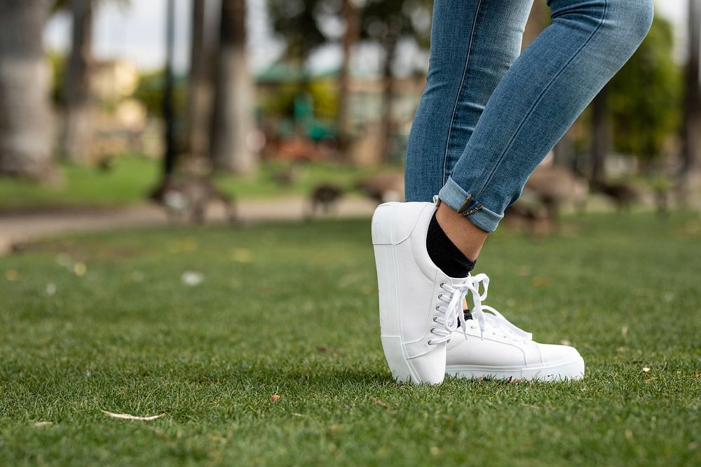 Woman in jeans wearing white sneakers at a park, casual footwear fashion