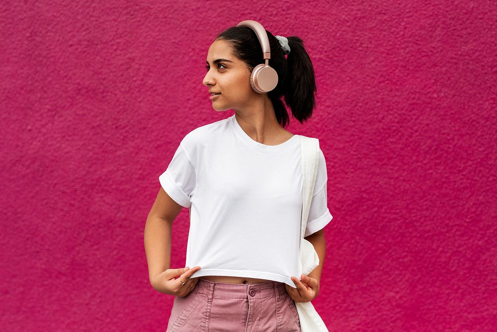 Hispanic woman in white tee listening to music from wireless headphones, pink wall background