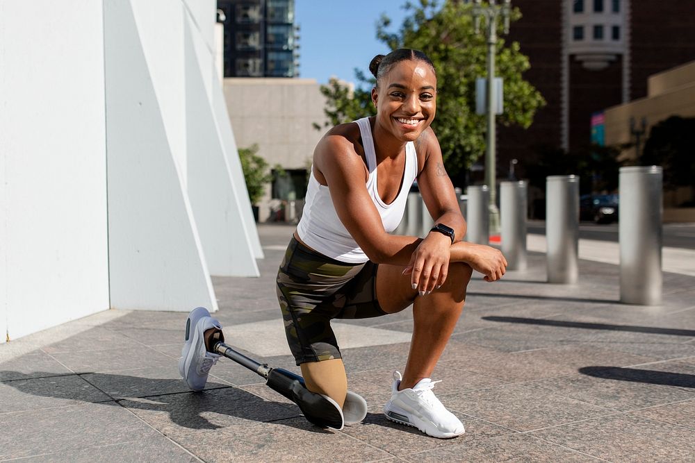 Smiling athlete with prosthetic leg kneeling down on the floor