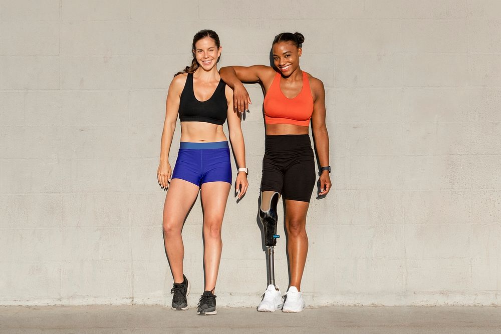 Two athletes, one with prosthetic leg, smiling by the wall