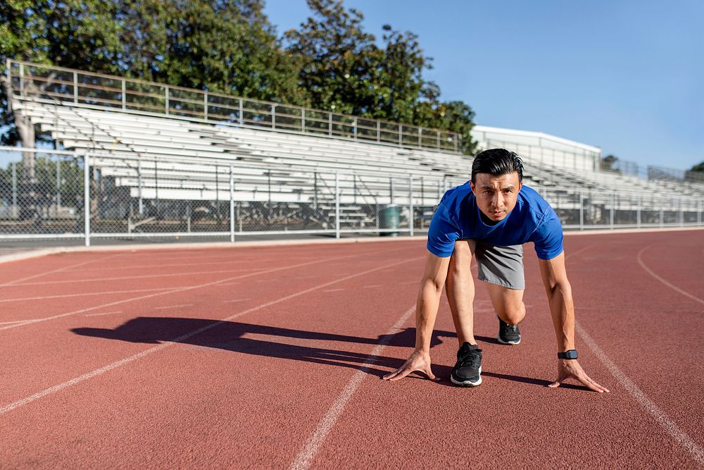 Asian man getting ready to take off on the running track