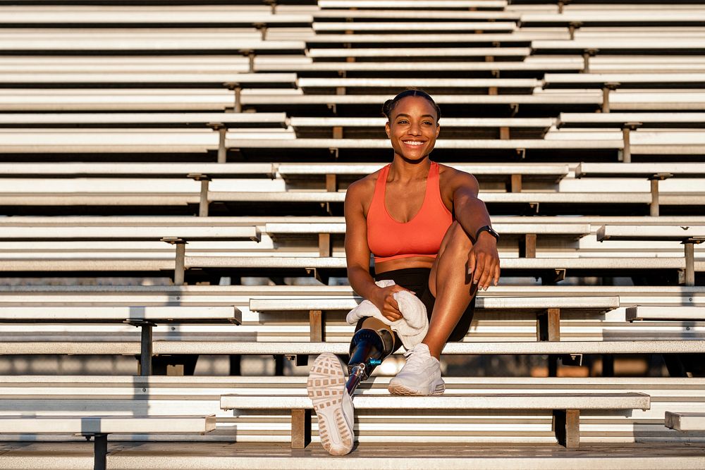 Woman athlete with prosthetic leg smiling carrying a towel and sitting to rest 
