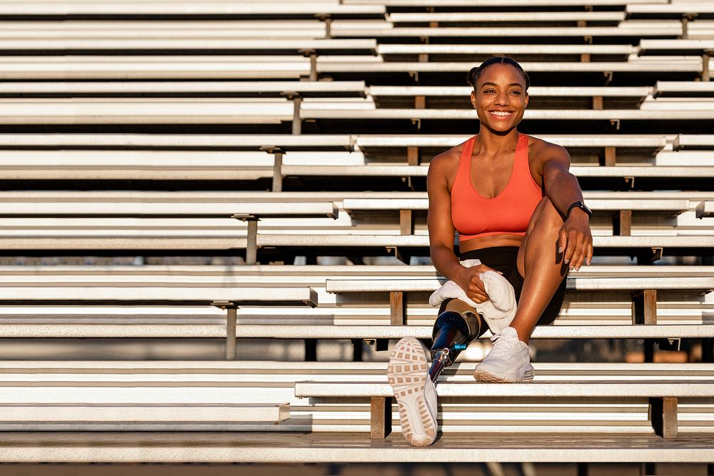 Woman athlete with prosthetic leg smiling carrying a towel and sitting to rest 