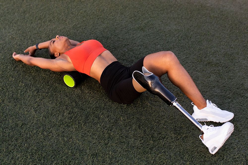 Woman athlete with prosthetic leg resting her back on a back roller