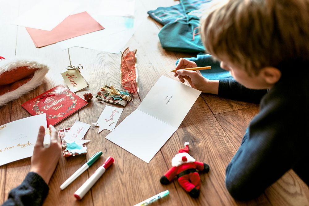 Kids writing Christmas cards on wooden floor