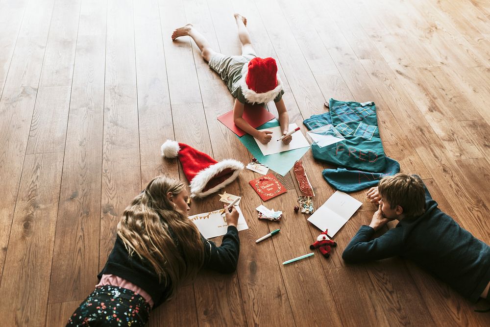 Kids writing Christmas cards on wooden floor