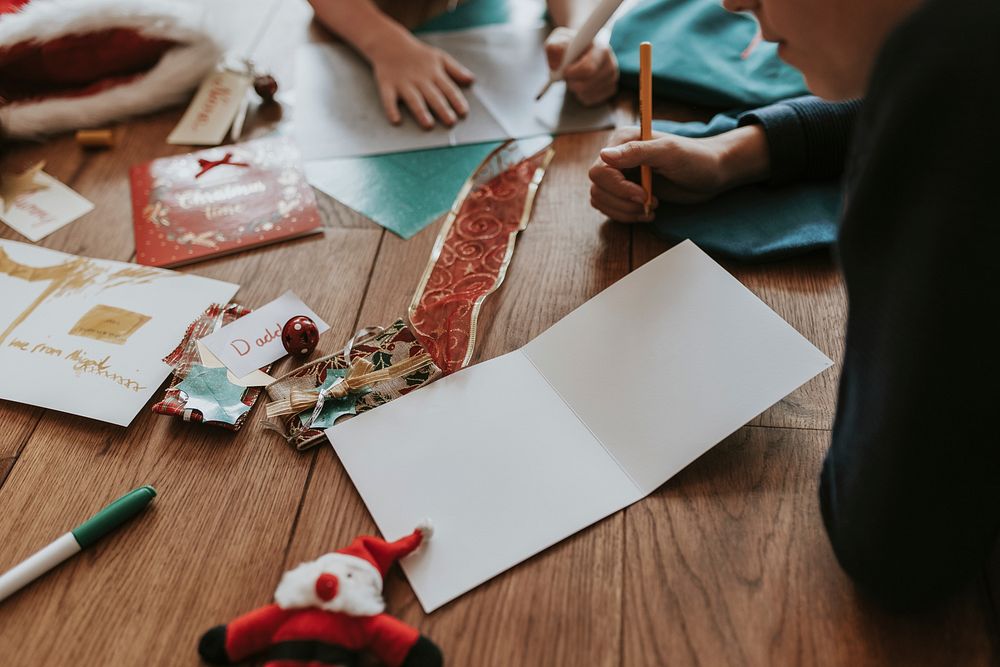 Kids writing Christmas cards on wooden floor