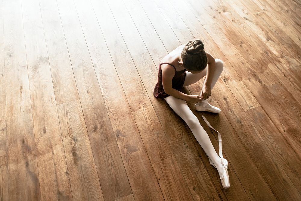 Ballerina background, young girl tying shoes on wooden floor