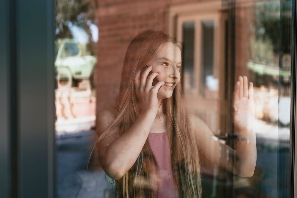 Young girl on the phone, hand touching glass window, the new normal
