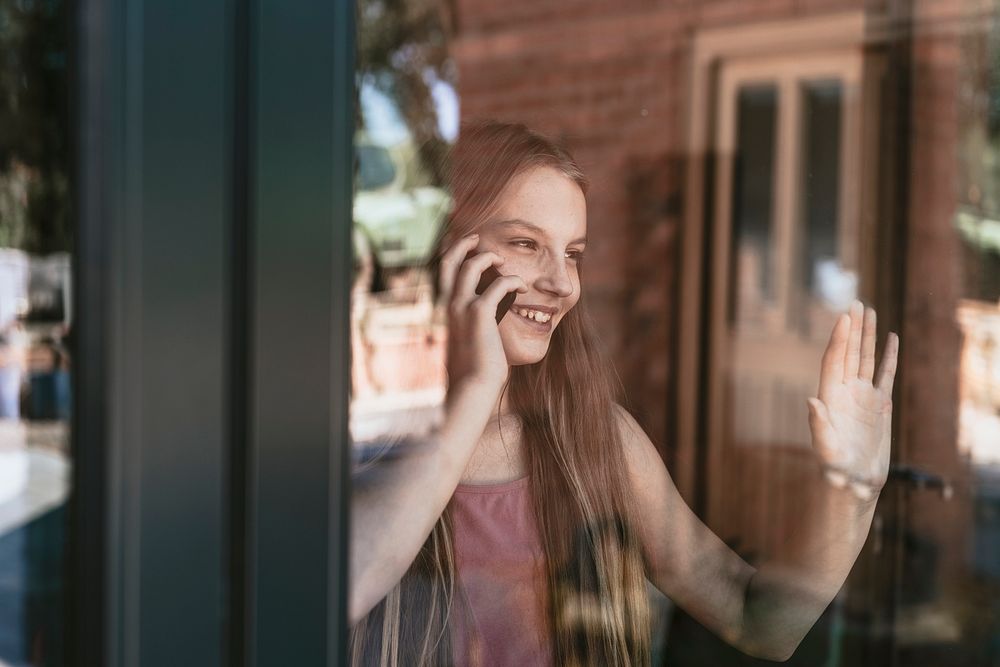 Young girl talking on the phone, hand touching glass window, the new normal