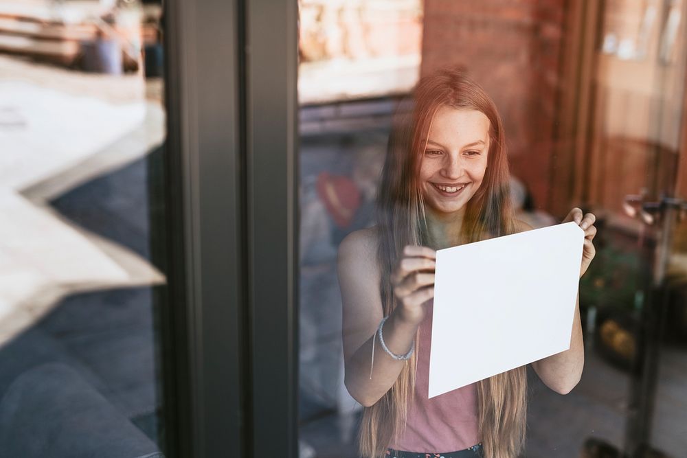 Blond girl showing blank paper sign through glass window, the new normal