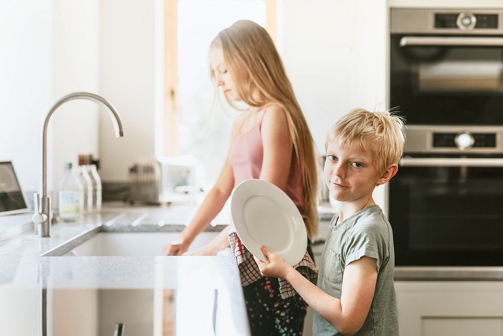 Young boy wiping dishes in kitchen, basic house chores