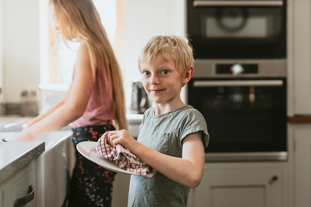 Young boy wiping dishes in kitchen, household chores for kids