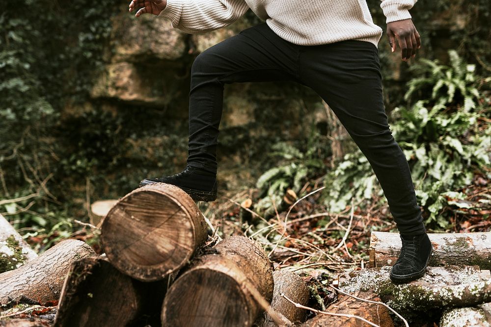 Man crossing stack of logs in woods