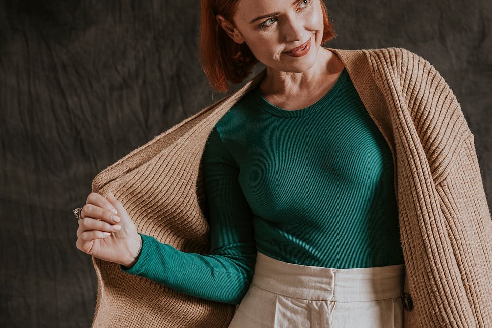 Happy woman putting on brown cardigan over green long sleeve, autumn apparel fashion design