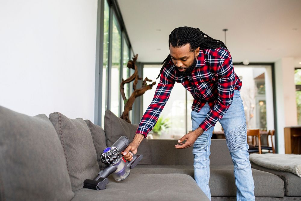 Man vacuuming sofa with a handheld Dyson vacuum cleaner. 20 NOVEMBER 2021 - LOS ANGELES, USA