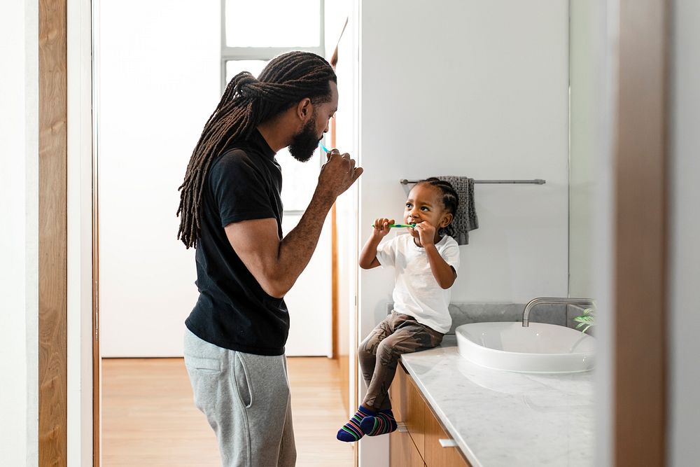 Boy learning to brush his teeth together with father