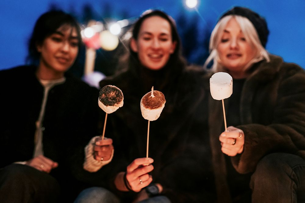 Friends enjoying s'mores and marshmellow together by the bonfire 