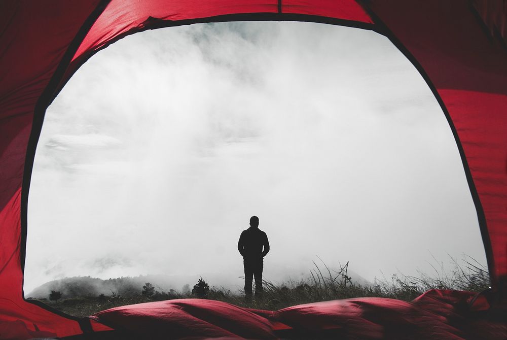 Man in front of a red tent amid the morning haze