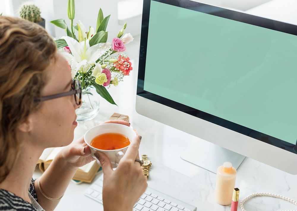 Woman drinking tea and staring at a mockup computer screen