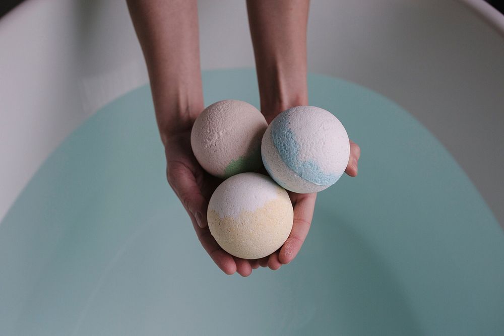 Three premium bath bombs being held in hands over a spa tub.