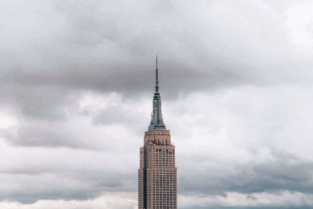 The top half of the Empire State Building scraping the sky on an overcast day.
