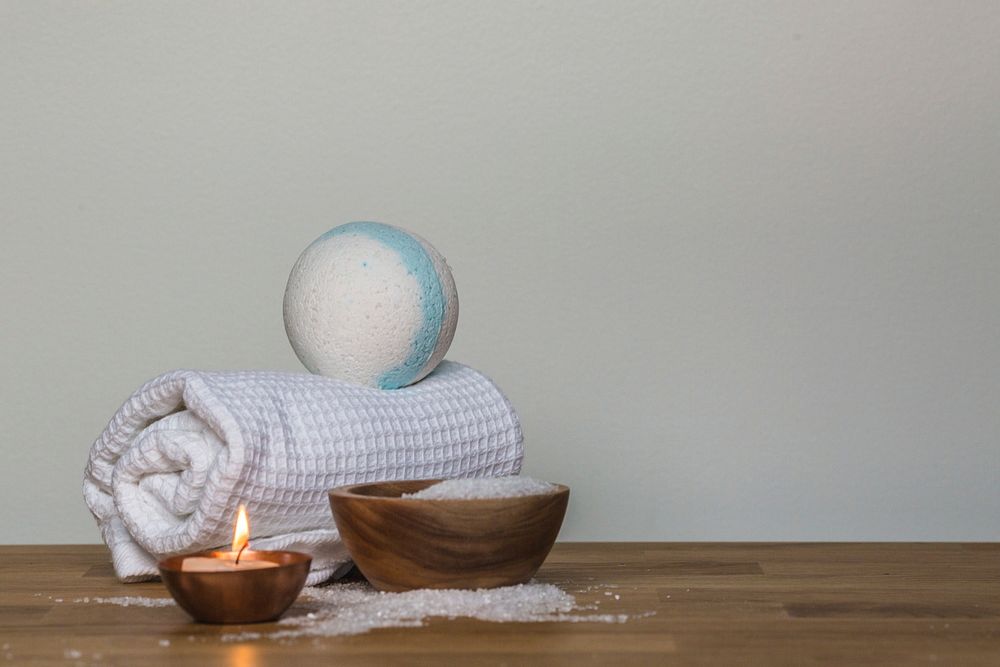 Blue and white bath bomb on white towel next to tray of epsom salt and lit candle.
