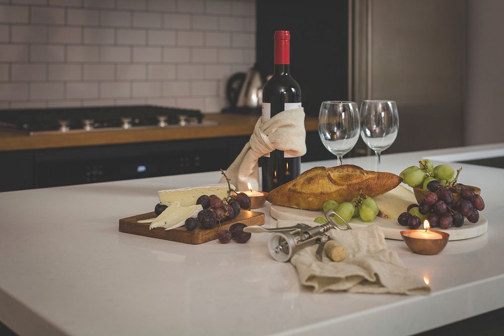 Free spread of wine, cheese, bread, grapes, wine glasses laid out on kitchen counter image, public domain food CC0 photo.