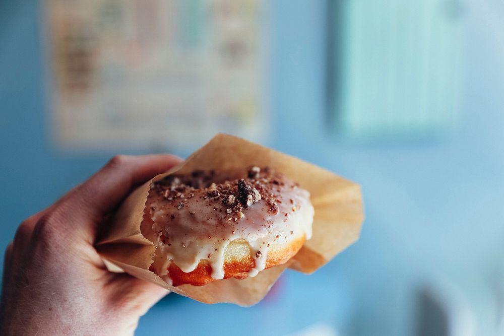 Free hand holding fresh donut in brown paper bag image, public domain food CC0 photo.