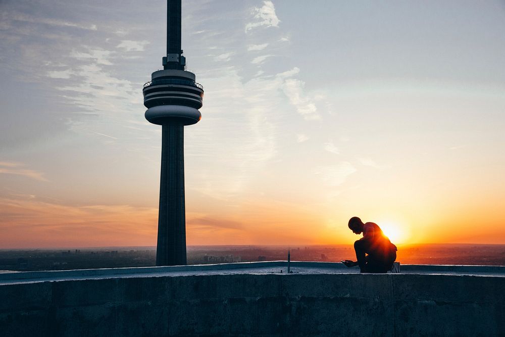 Man on rooftop of building with sunrise behind CN tower in Canada.
