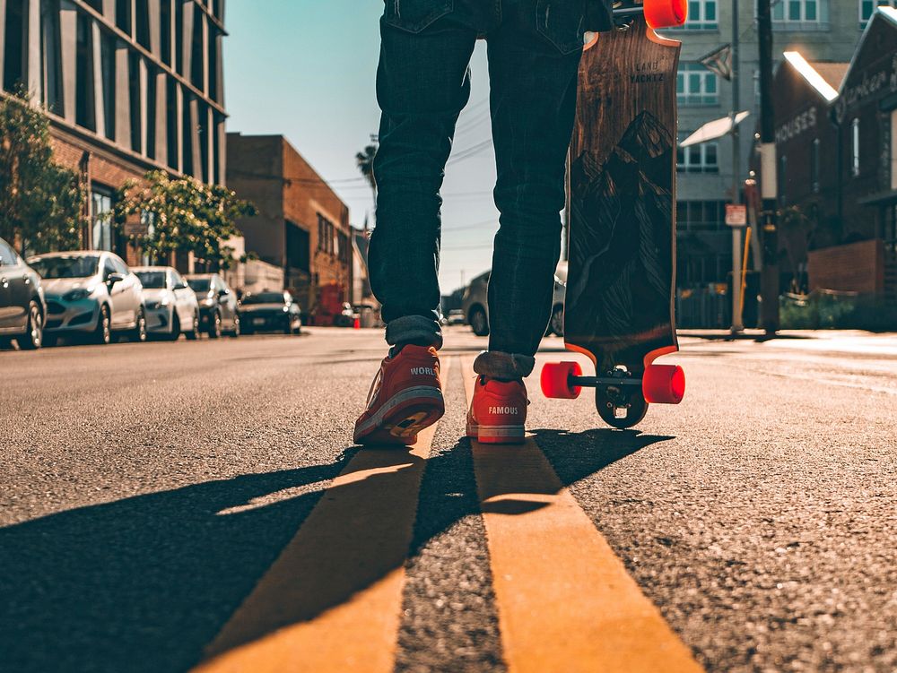 Back view of a longboarder holding a skateboard on a city street.