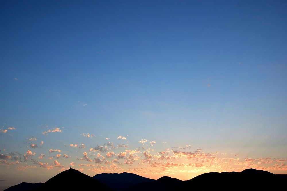 Clouds over mountain tops are lit up by a sunset.