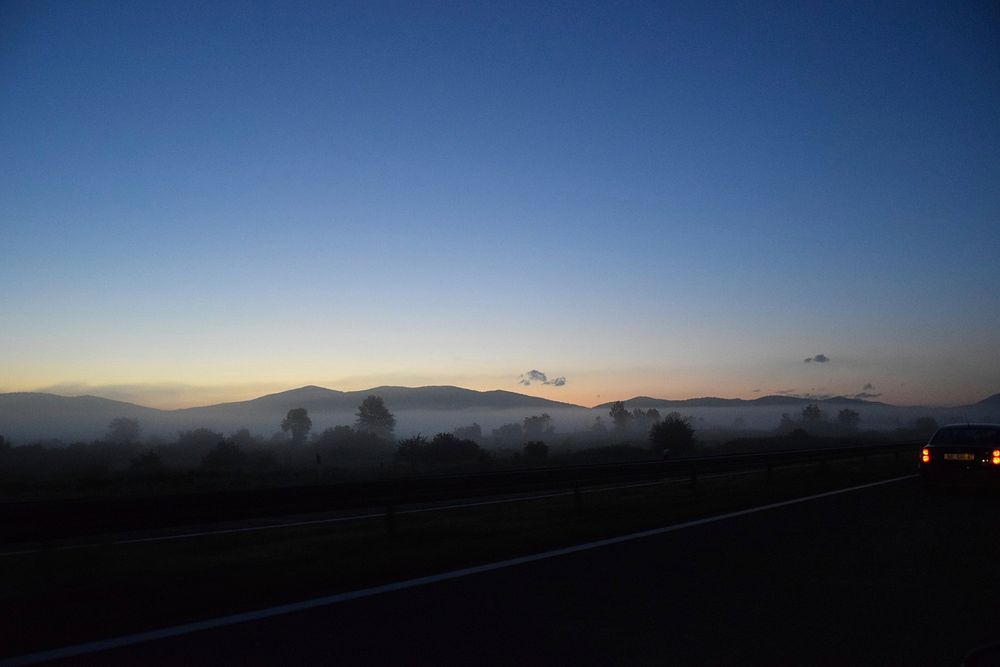 View of a hillside by a highway through the fog at sundown.